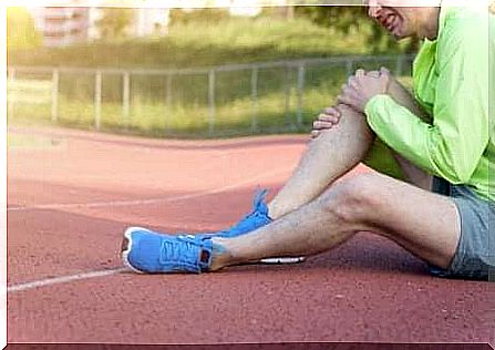 Sportsman sits on cinder track and holds his knee